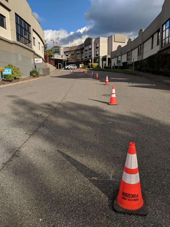 Asphalt road with orange and white traffic cones, flanked by buildings under a partly cloudy sky.