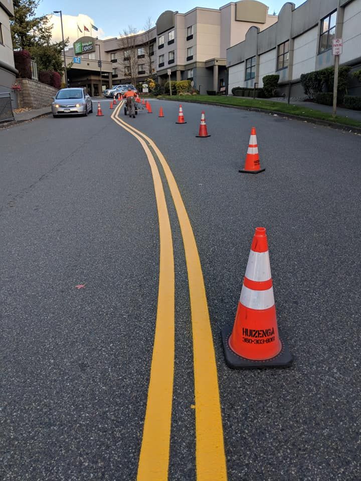 Road with yellow lines and orange cones. A car and a person are in the distance.