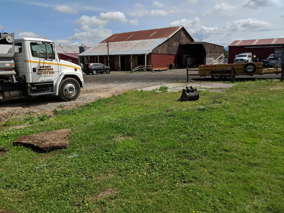 White dump truck, tractor trailer, barns, and trailer on green grassy land, sunny day.