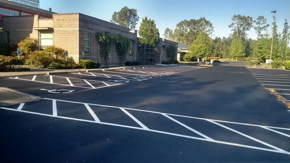 Exterior view of a newly paved parking lot with marked handicap spaces in front of a brick building.