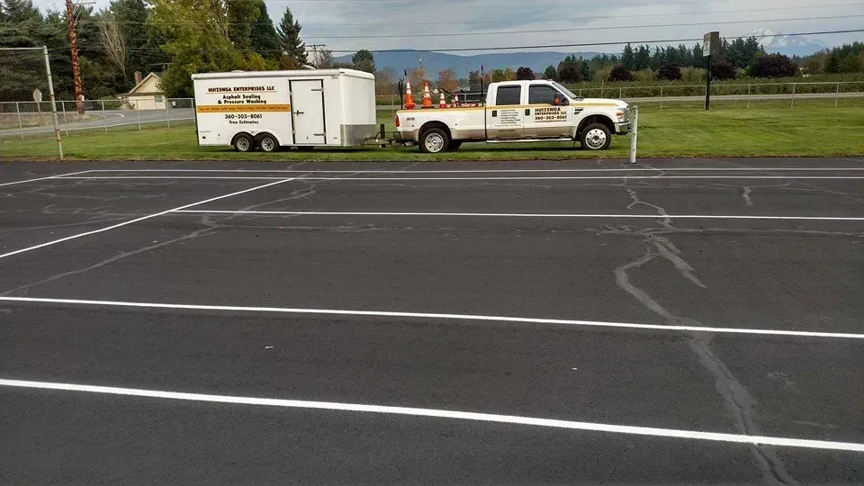 White truck with trailer parked on asphalt, striping crew onsite with cones.
