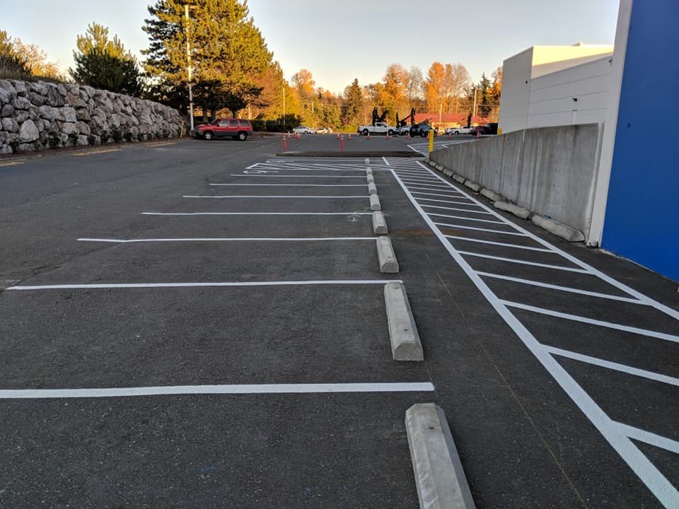 Parking lot with marked spaces and concrete bumpers. Cars in the distance, blue building on the right.