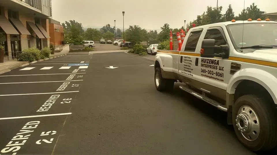 White truck parked on a paved lot with reserved parking spots. Building and other vehicles in the background. Hazy sky.