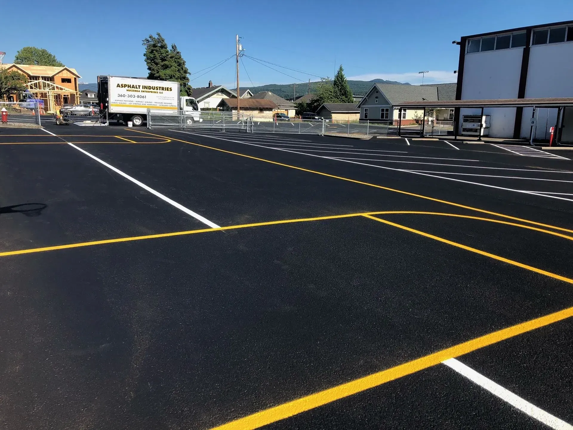 Newly paved parking lot with painted yellow and white lines. Buildings and truck in the background.