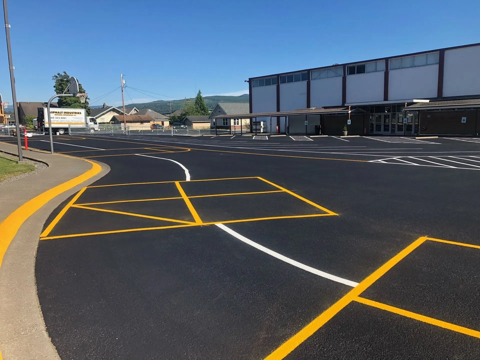 Asphalt parking area with yellow and white painted lines near a school building, sunny day.