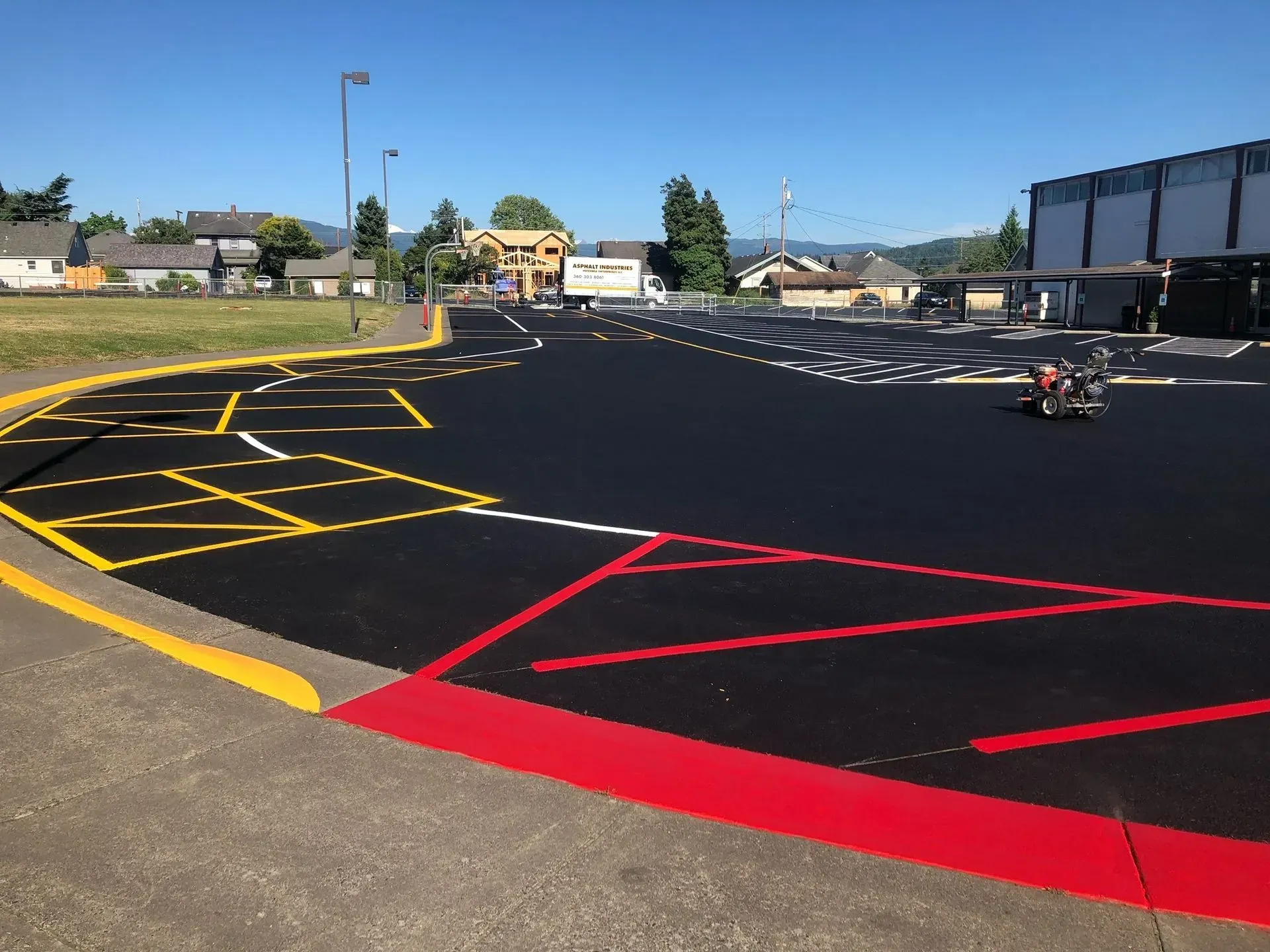 Black asphalt parking lot with yellow, white, and red markings. Buildings and trees are in the background.