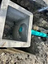 Concrete box in a dirt trench, connected to a turquoise pipe. Construction or utility context.