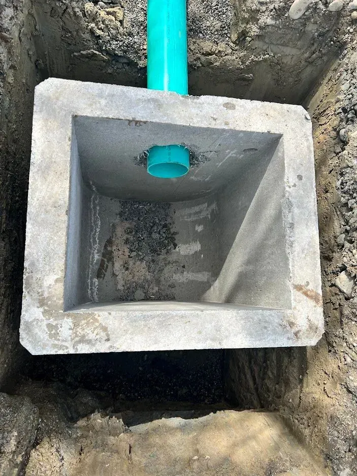 Concrete box with a green pipe in a dug-out hole, possibly for drainage.