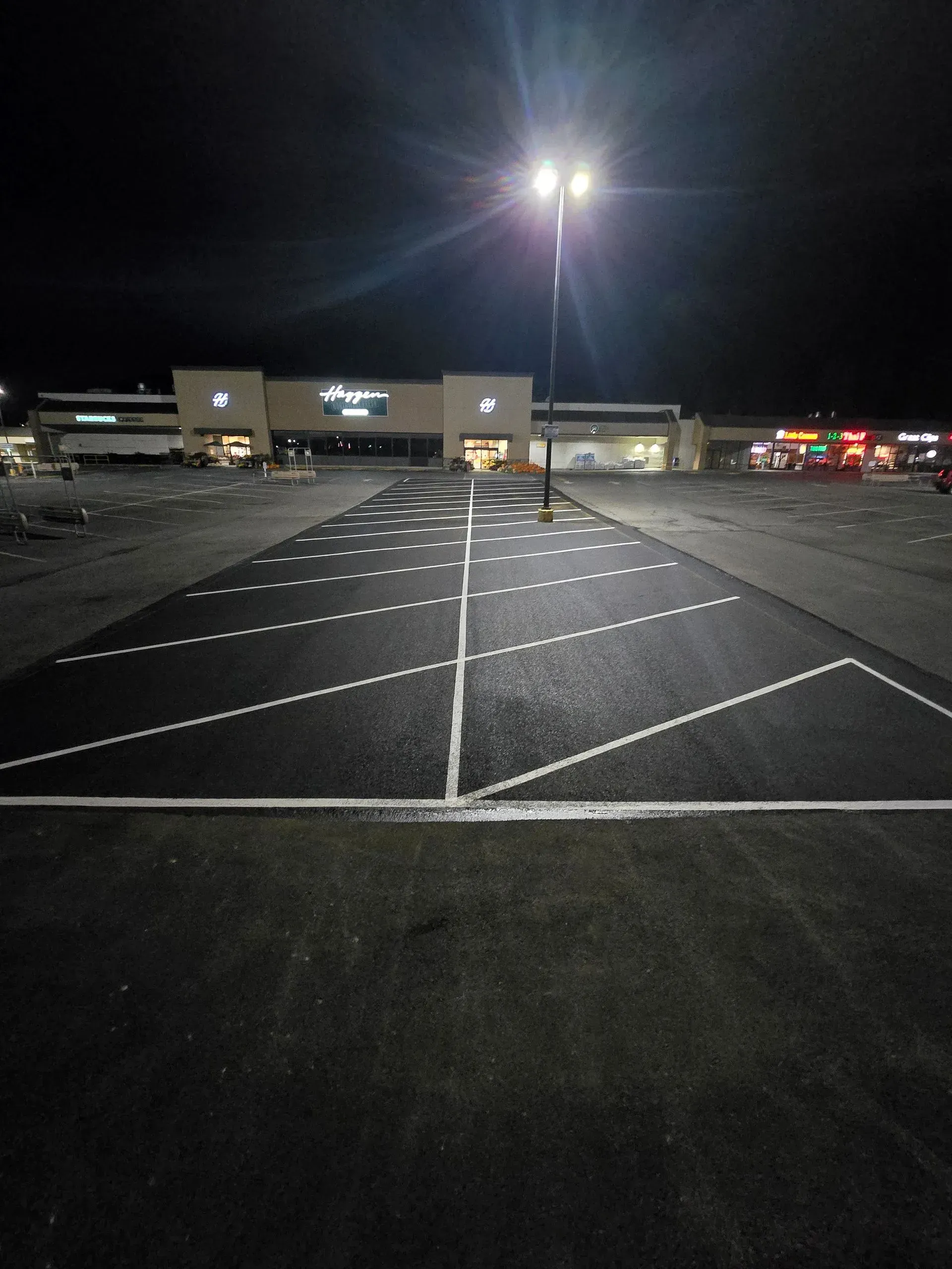 Dark parking lot at night, newly paved with white parking space lines. Bright streetlights illuminate the scene.