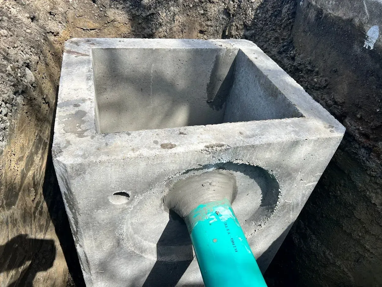 Concrete square structure with green pipe in a dirt trench.