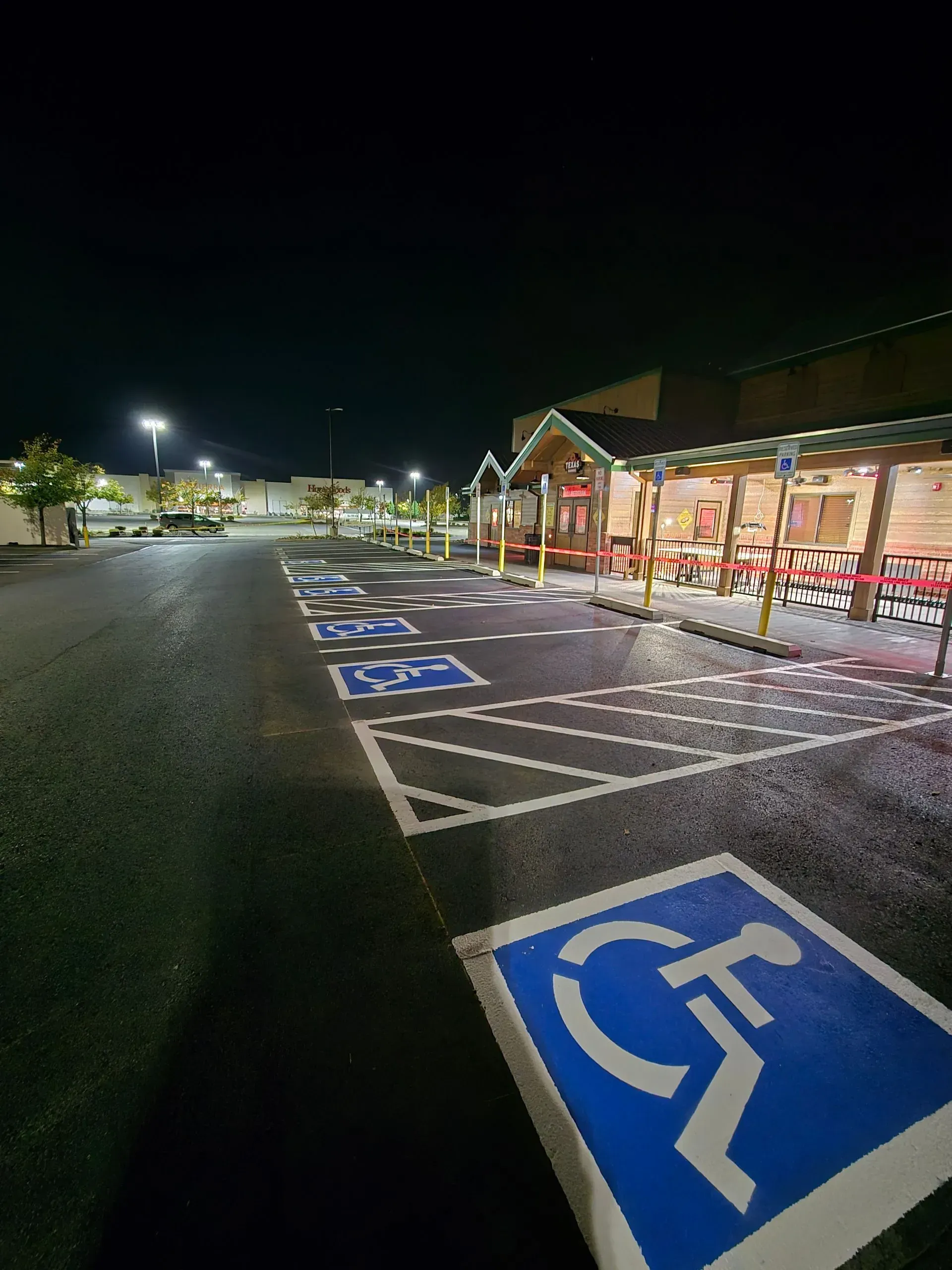 Nighttime view of a parking lot with several marked accessible parking spaces near a restaurant with a red awning.