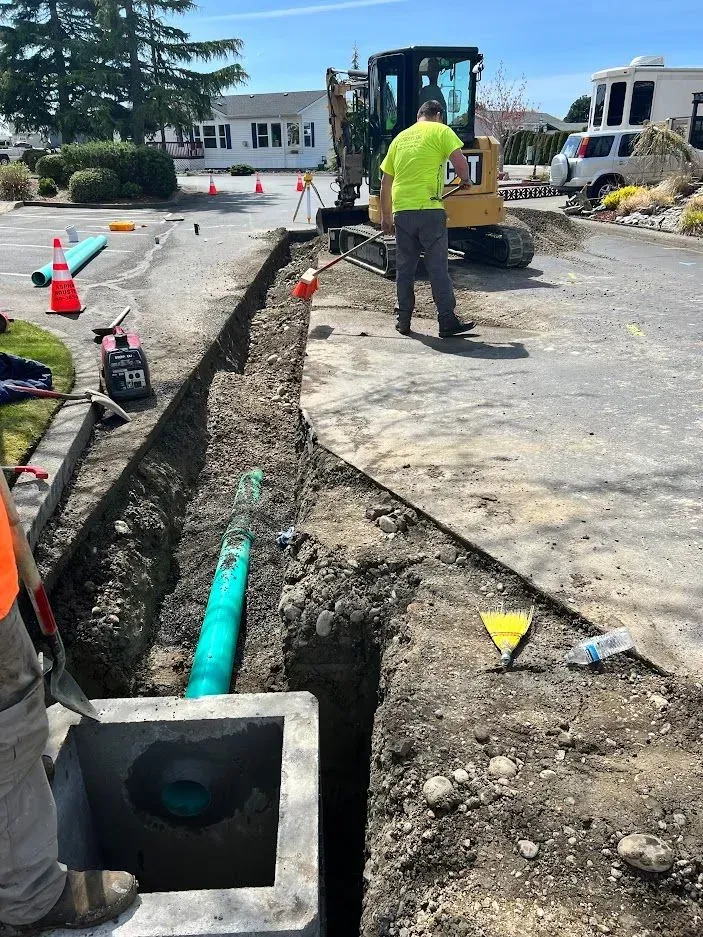 Construction site: Workers with excavator digging a trench, laying green pipe.