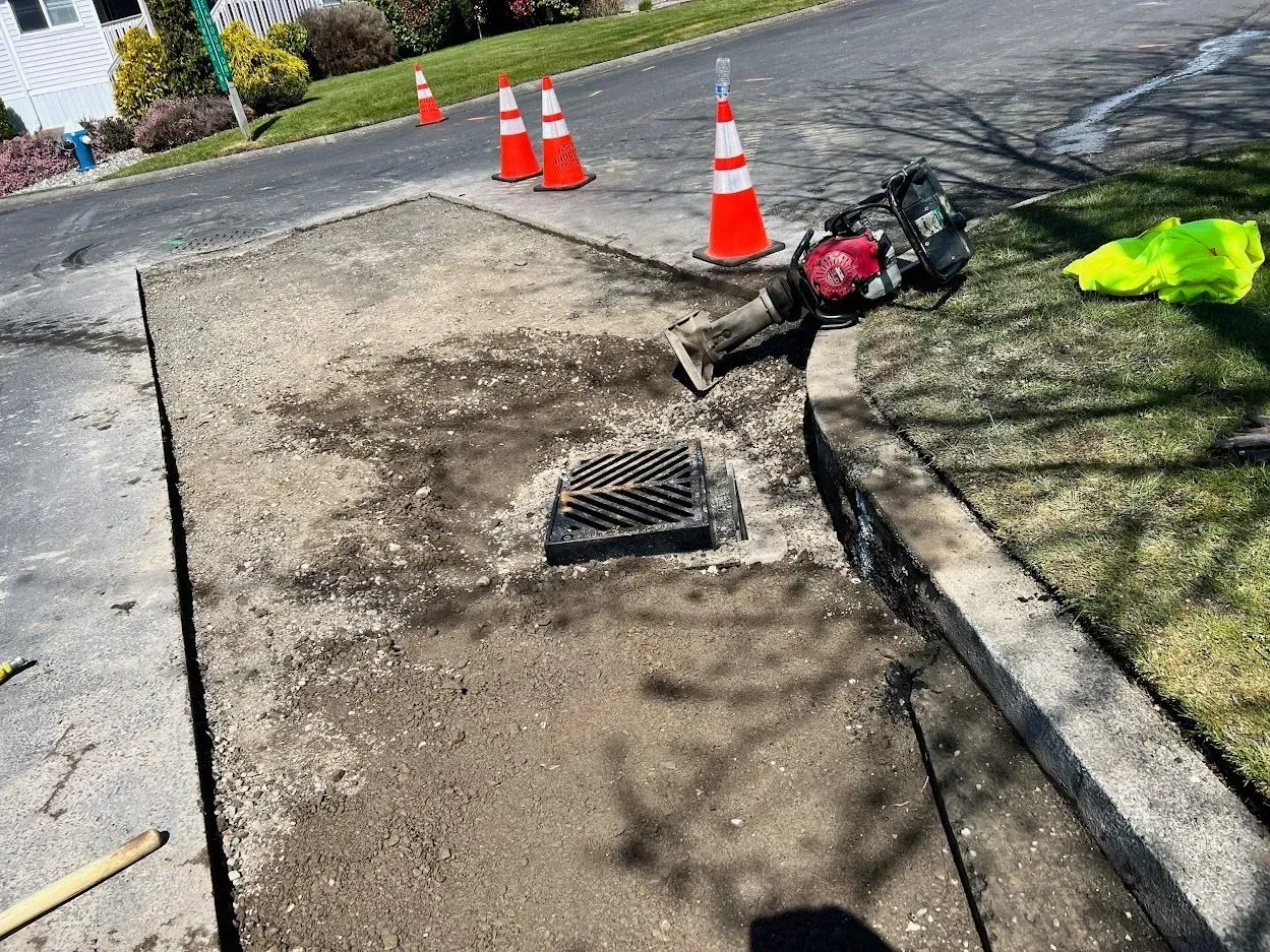 Road work: drain repair in progress, with orange cones, debris and tools on asphalt.
