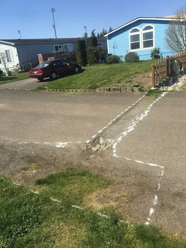 Asphalt road intersection with grass, a red car, and blue and gray houses.