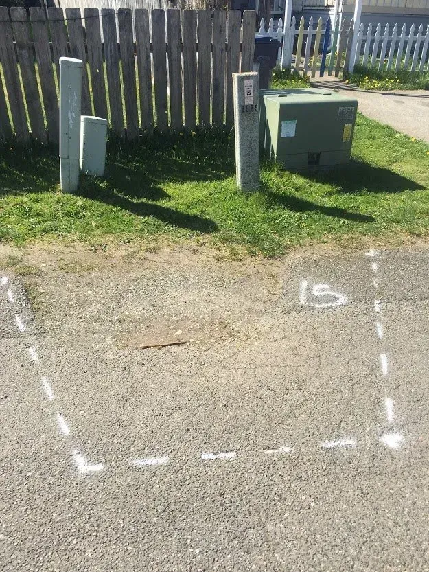 Asphalt ground with a white-dashed square, power poles, a utility box, and a wooden fence on grass.