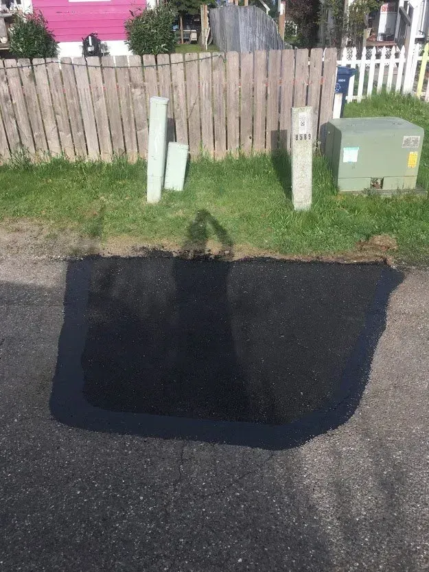 Patch of black asphalt on a street; utility poles and a fence in the background.