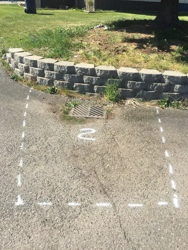 Asphalt parking space outlined in white paint, near a decorative stone retaining wall and grassy area.