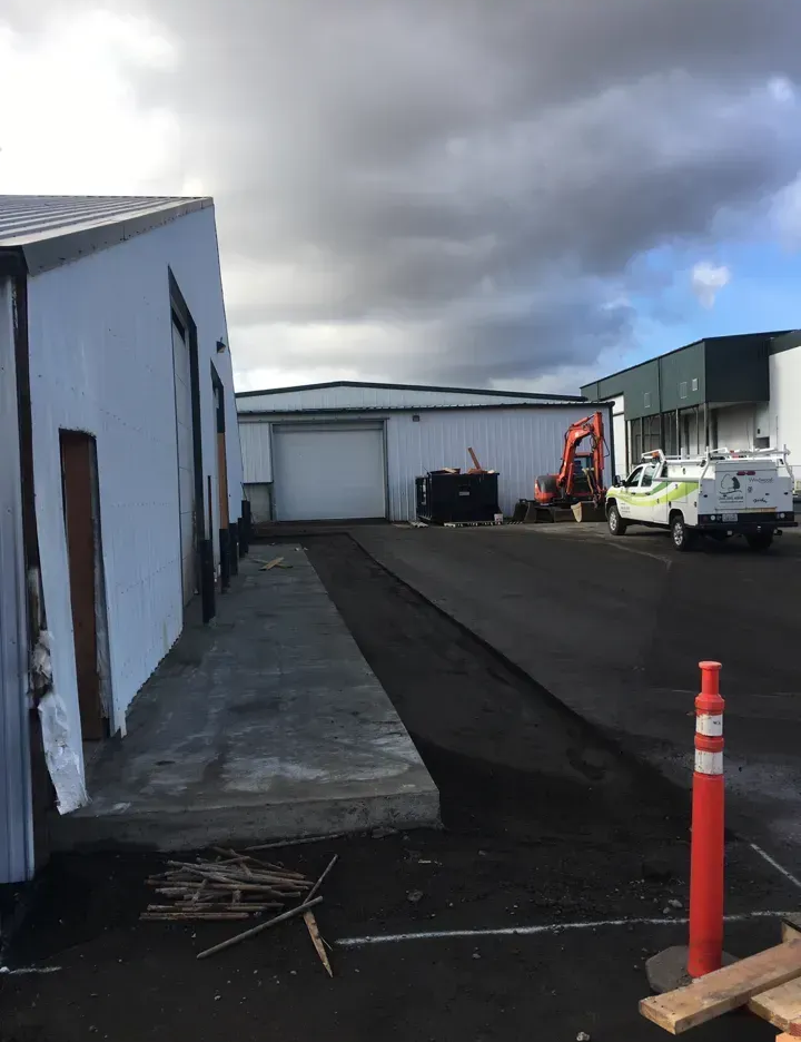 Exterior of industrial buildings, asphalt and concrete driveways, construction equipment, cloudy sky.