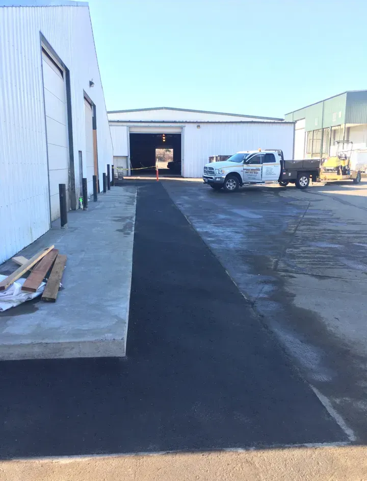 Asphalt path between two white industrial buildings with a parked pickup truck.