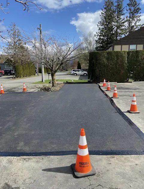 Freshly paved asphalt parking area with orange traffic cones under a bright blue sky.