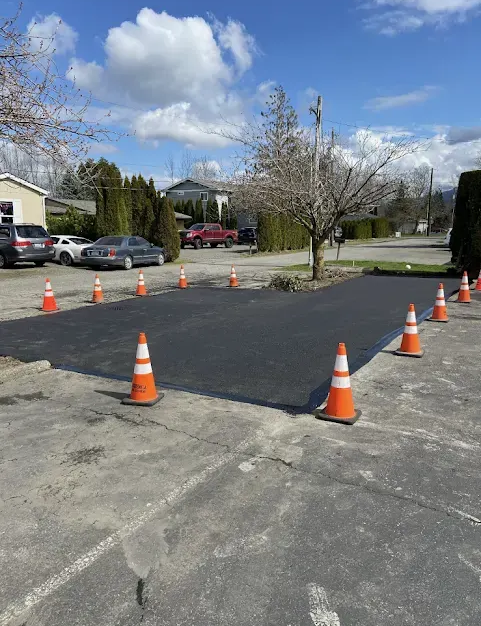Freshly paved asphalt patch surrounded by orange traffic cones in a parking lot.