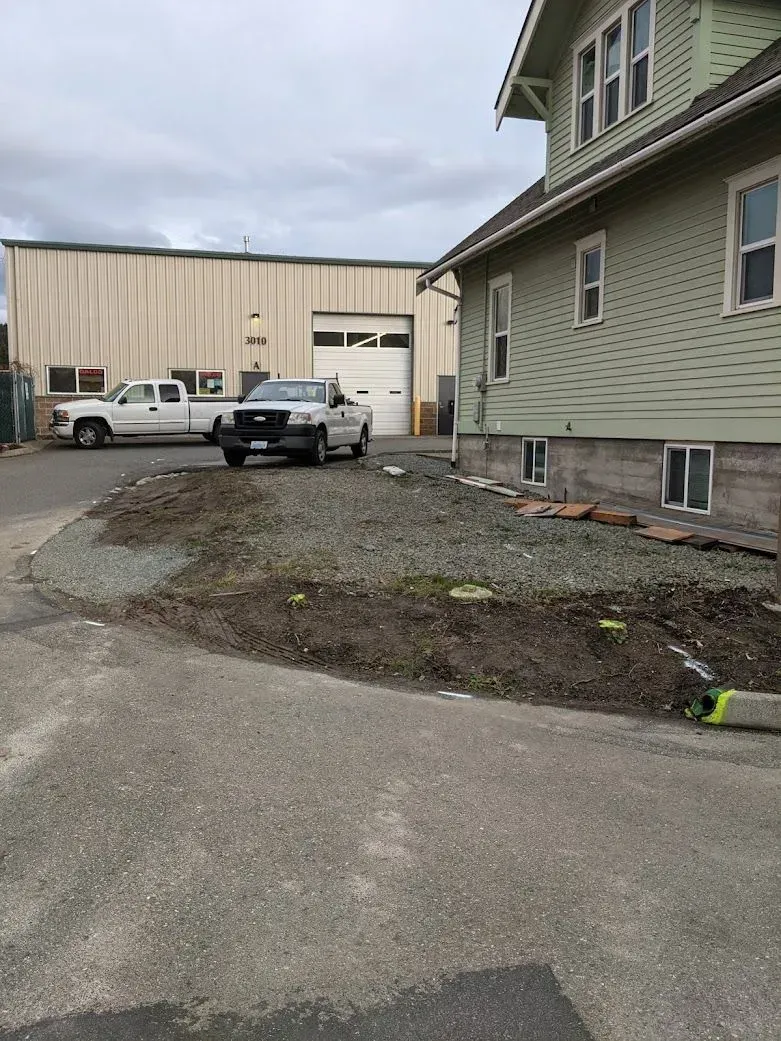 Two trucks parked near a building and garage. Gravel area in foreground. Overcast sky.