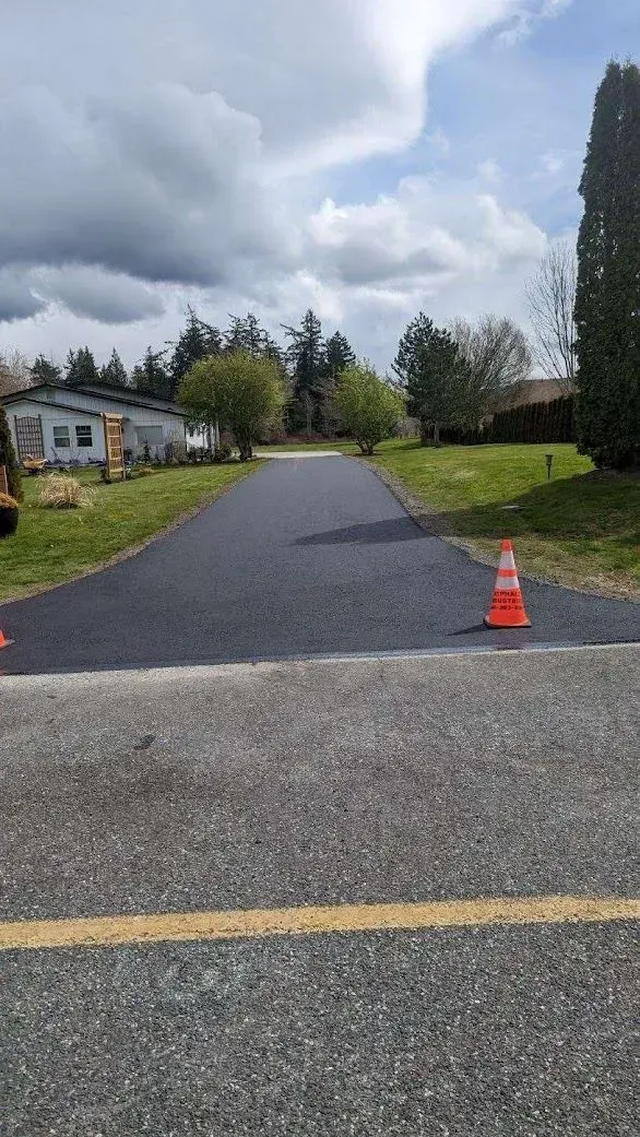 Newly paved asphalt driveway leading toward homes, marked by orange cones and flanked by grass.