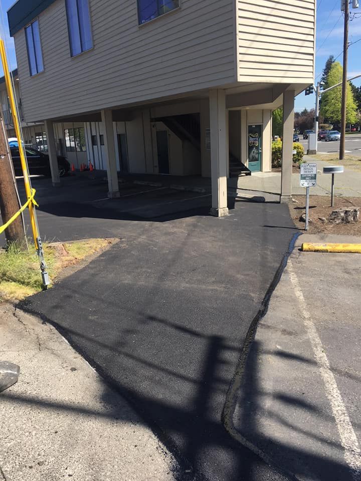 Newly paved asphalt leading to a building with elevated foundation. Yellow caution tape and a mailbox are present.