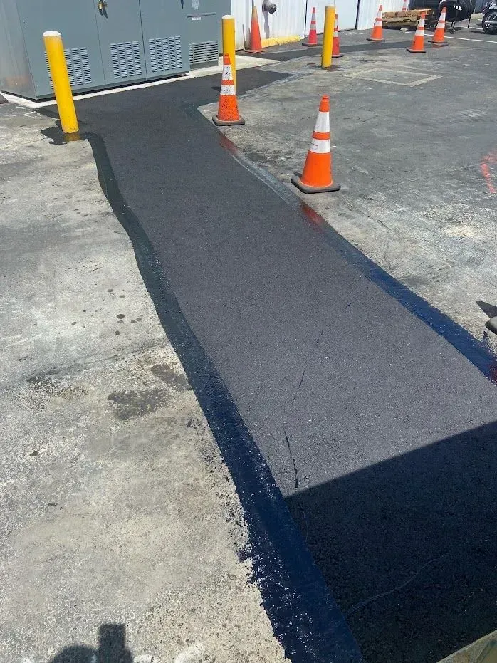 Newly paved asphalt pathway in a parking lot, with orange cones for safety.
