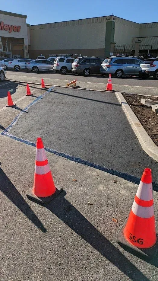 New asphalt patch in a parking lot, marked with orange cones and blue lines, near a Meijer store.