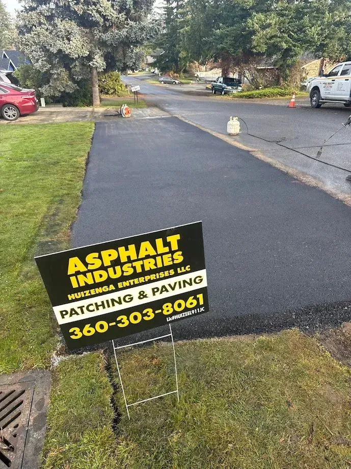 Newly paved asphalt driveway with sign for Asphalt Industries.