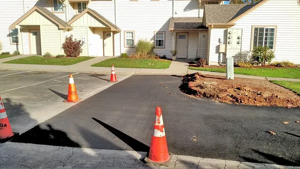 Asphalt parking area with orange traffic cones, next to a building with a walkway.