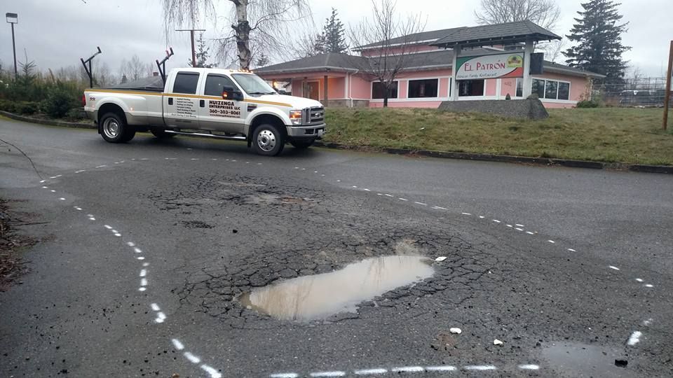 White pickup truck on a pothole-ridden road, in front of a building with a red sign.