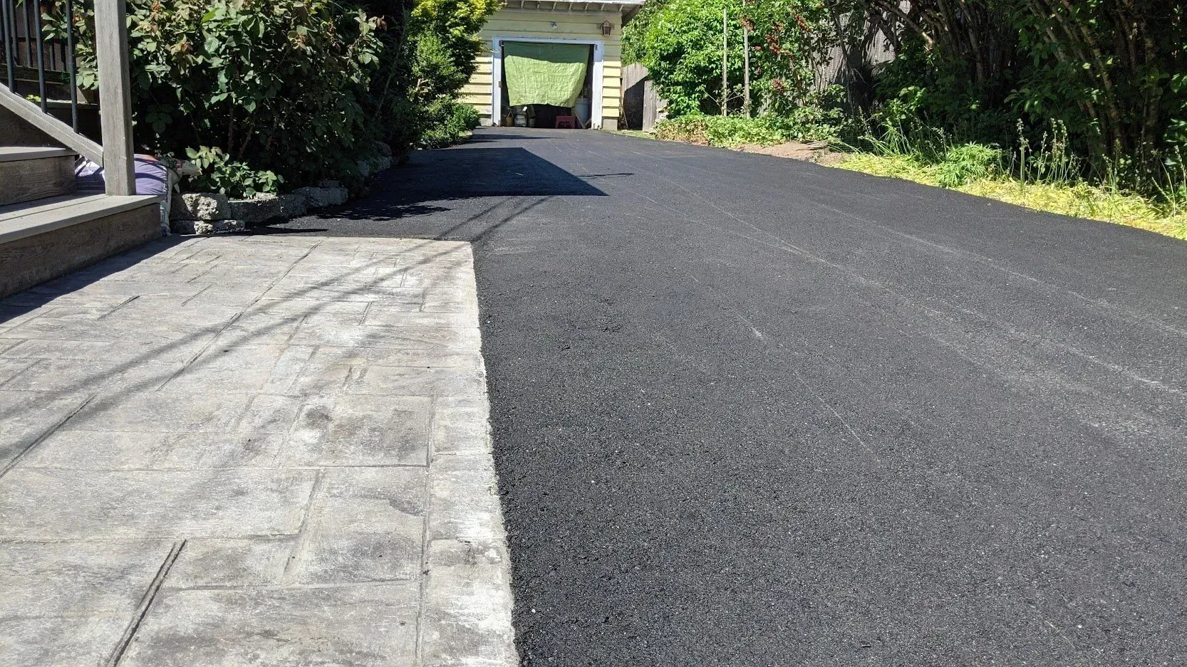 Asphalt driveway next to a stone walkway leading towards a garage.