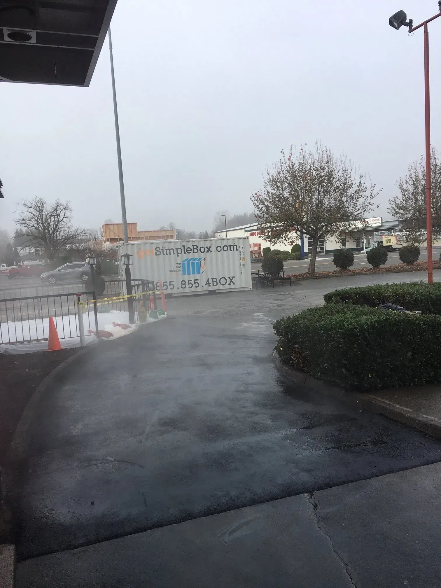 Exterior view of a business entrance; wet, dark pavement, a sign, bushes, and a cloudy sky.
