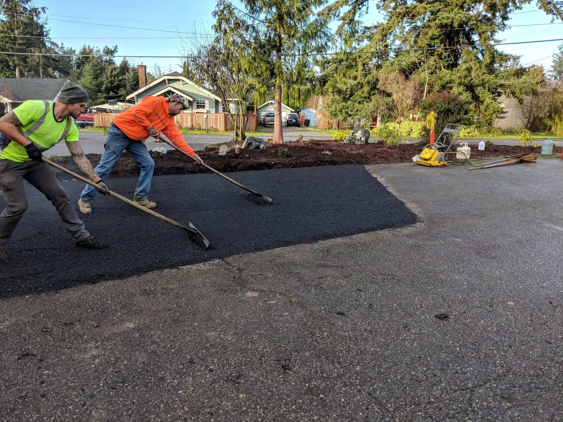 Two workers smoothing asphalt with rakes on a driveway.