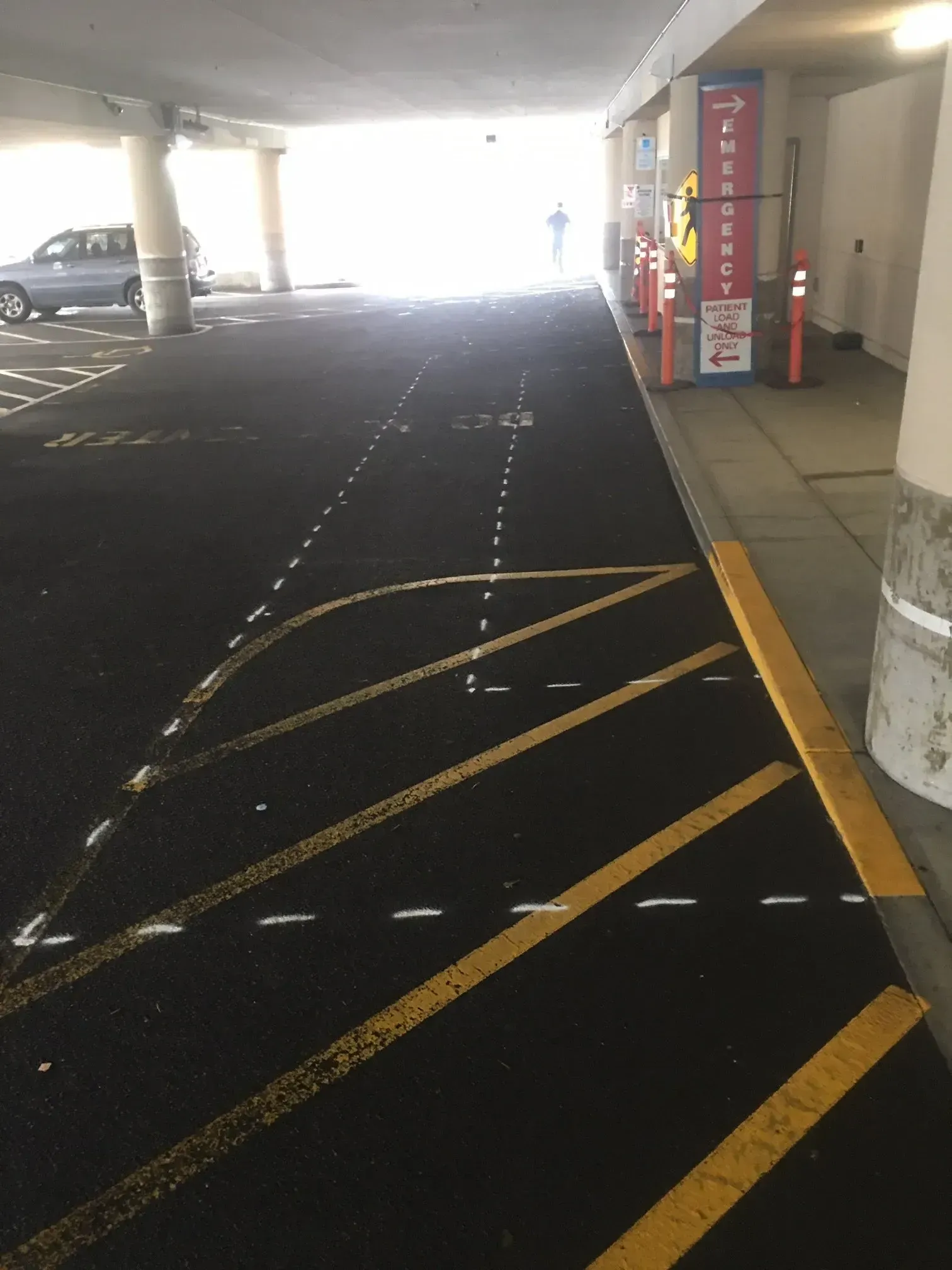 Parking garage interior with directional lines, yellow curb, and person walking toward exit.