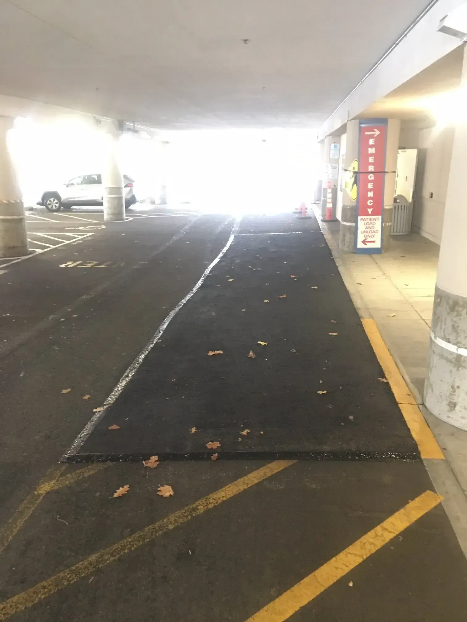 Driveway entrance to a parking garage with bright light at the end, lined with yellow markings.