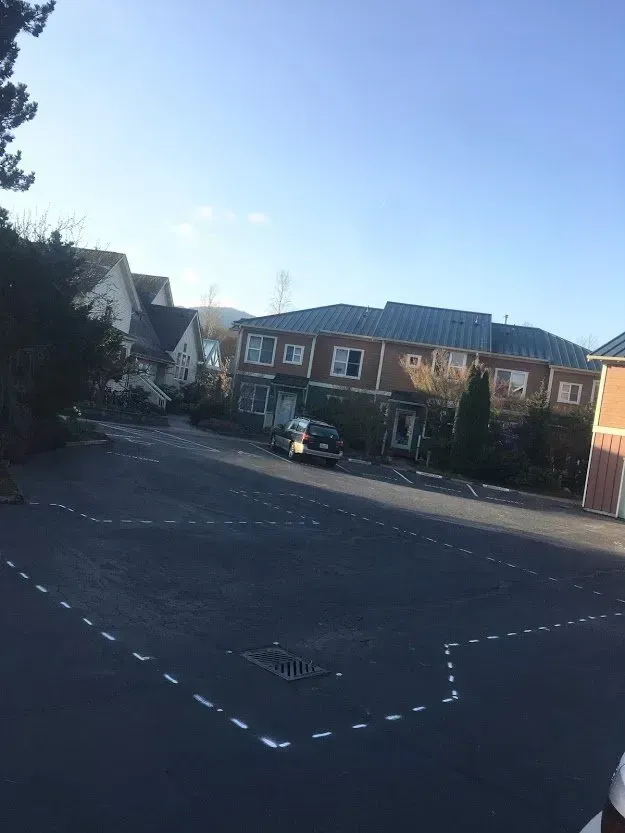 A car parked in a paved lot in front of brick buildings on a sunny day.