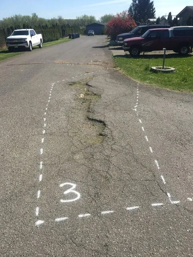 Asphalt road section marked with white lines, cracked and crumbling, with number