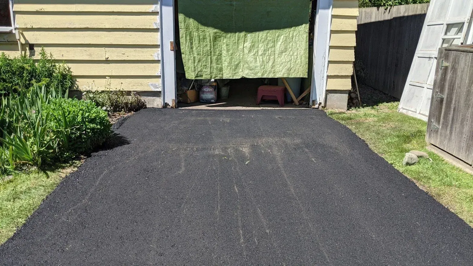 Freshly paved black asphalt driveway leading to a garage with an open door.