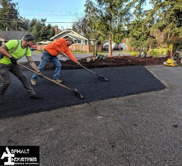 Two workers spread asphalt on a driveway with rakes.