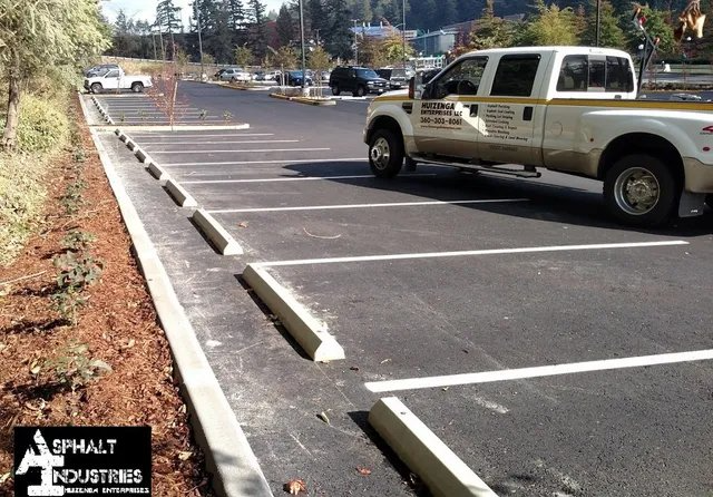 Parking lot with a white truck parked in a space; concrete wheel stops and painted lines.