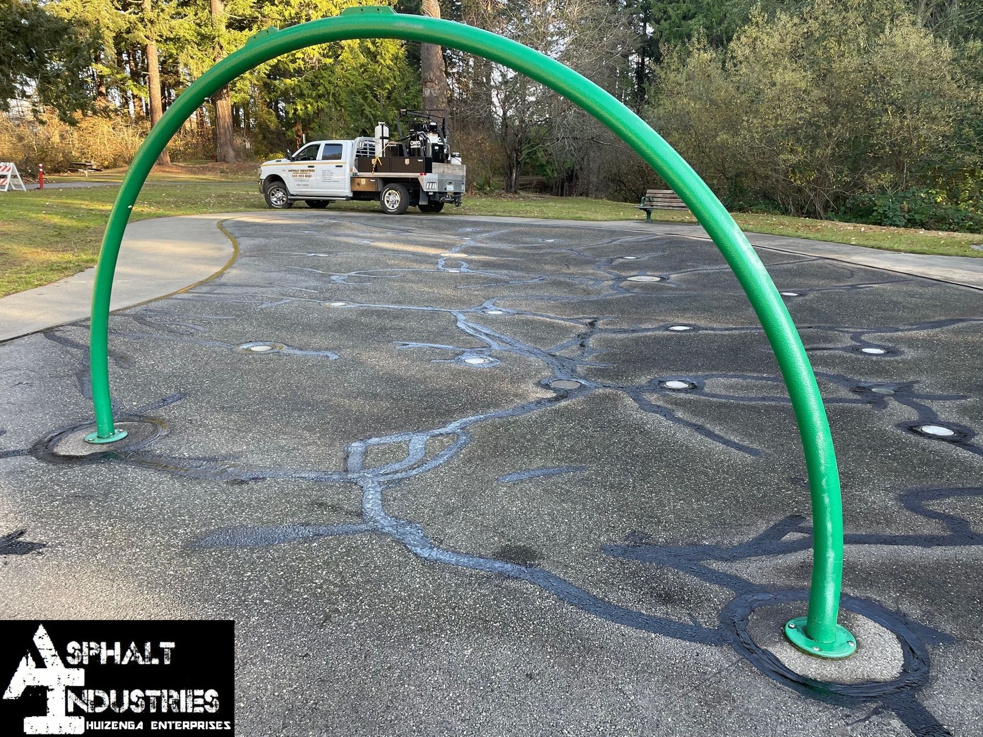 Green arch water feature in a park. A white truck is in the background.