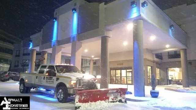 A snowplow truck clearing snow from an entrance to a hotel at night with blue lights.