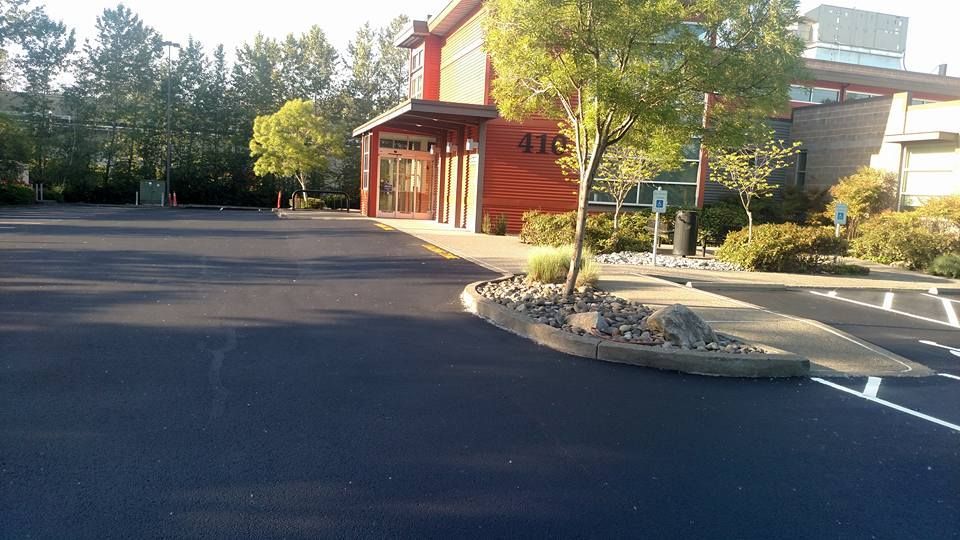 Exterior view of a building with a newly paved parking lot, trees, and landscaping. The building has orange siding.