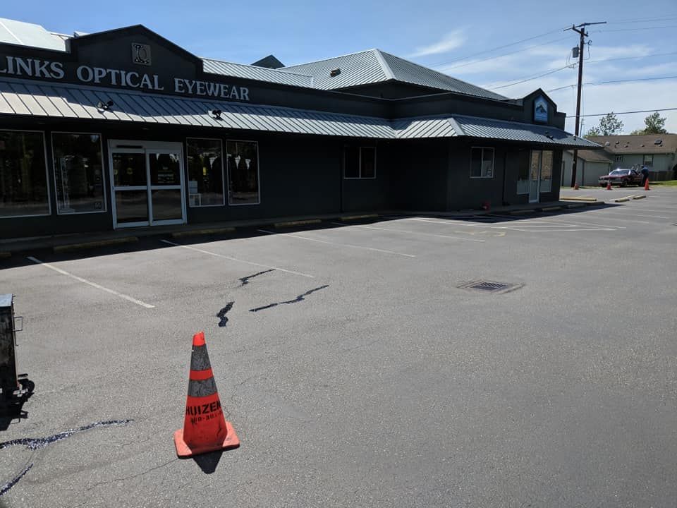 Exterior of Inks Optical Eyewear building with orange traffic cone in cracked parking lot on a sunny day.