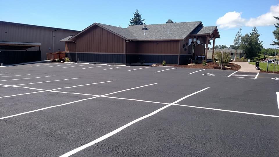 Empty parking lot in front of a brown building with a gray roof and blue sky.