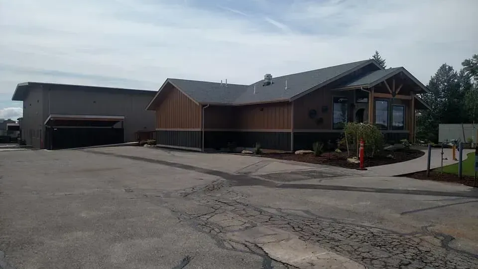 Modern building with dark gray roof, brown siding, and paved driveway.