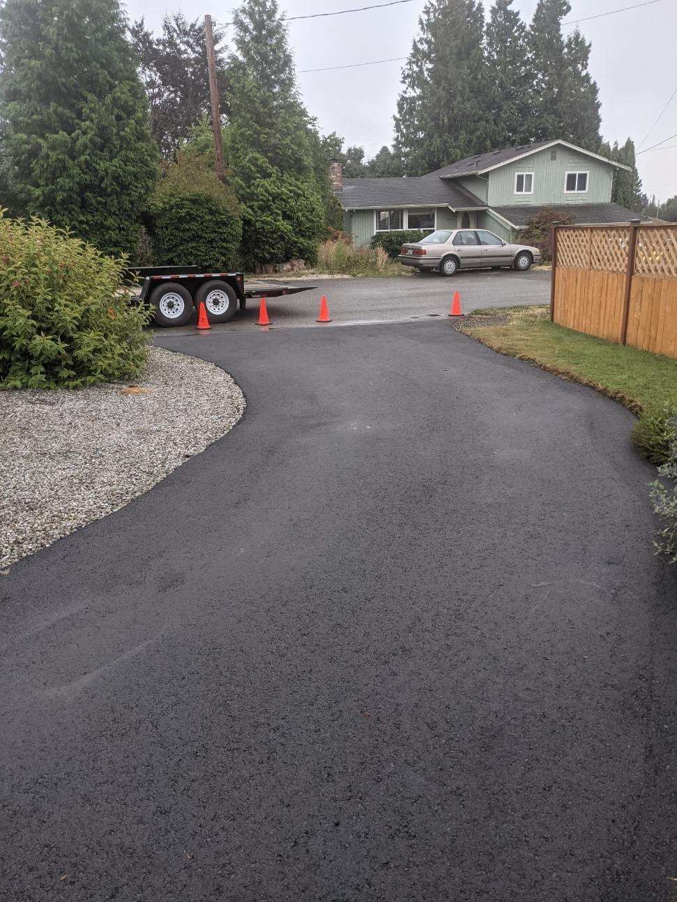 Newly paved asphalt driveway leading to a house, with a parked car and trailer.